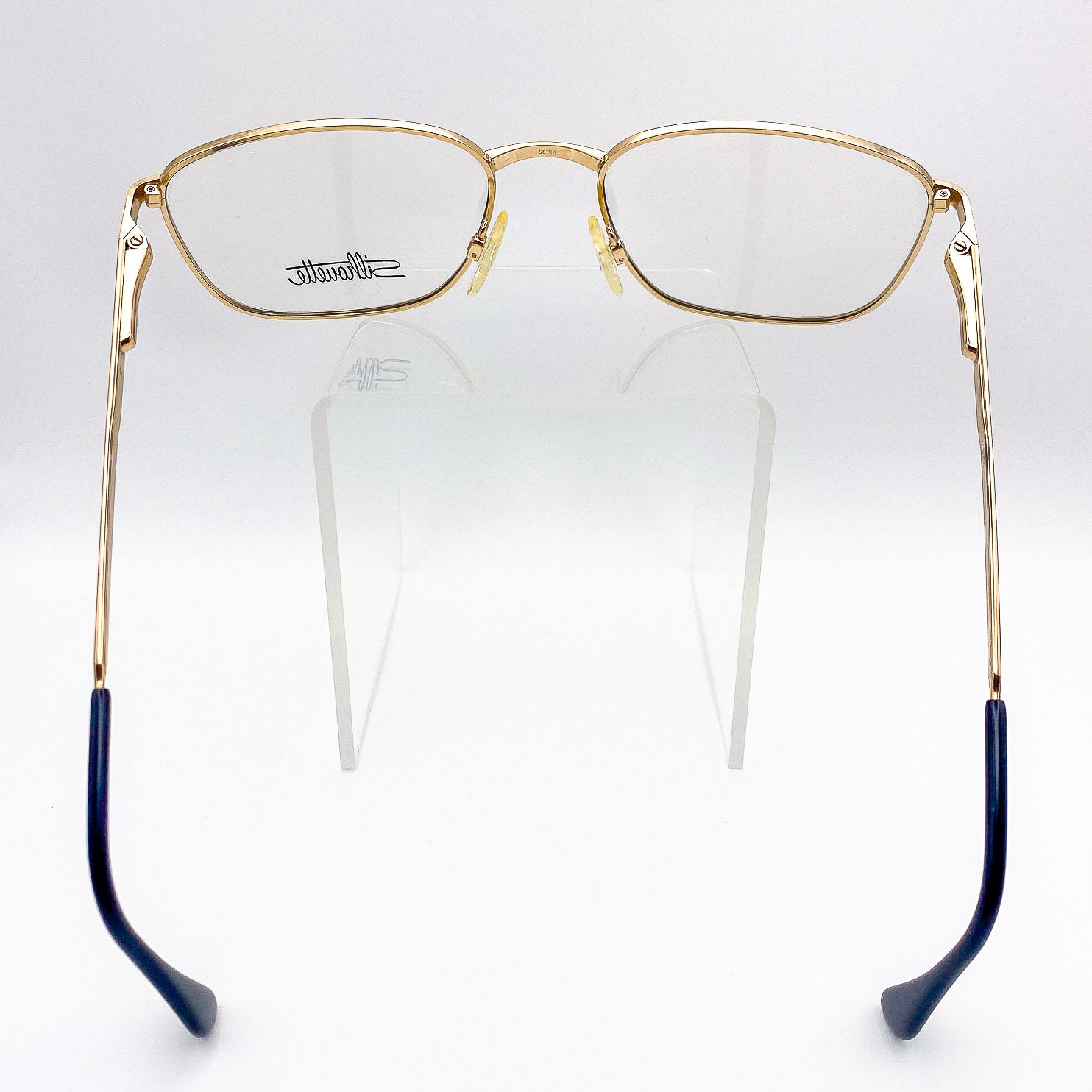 vintage 1990s Silhouette gold eyeglasses frames on a clear stand