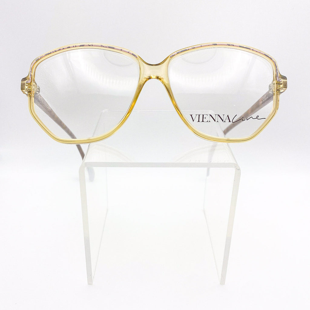 Gold-framed eyeglasses on a white stand with 'VIENNA' branding.
