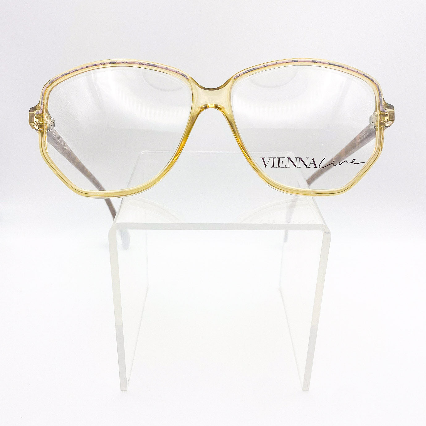 Gold-framed eyeglasses on a white stand with 'VIENNA' branding.