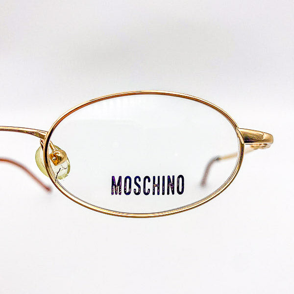 Gold-framed eyeglasses with 'Moschino' logo on a white background
