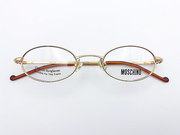 Vintage gold-framed eyeglasses with 'Moschino' branding on a white background