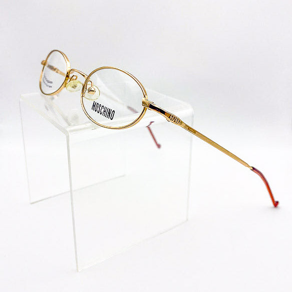 Gold-framed oval eyeglasses with branding on a white background