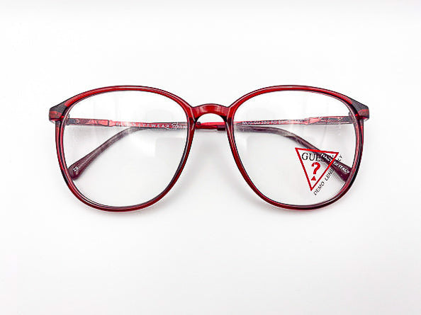 1980s translucent red eyeglasses with a visible Guess brand logo on a white background
