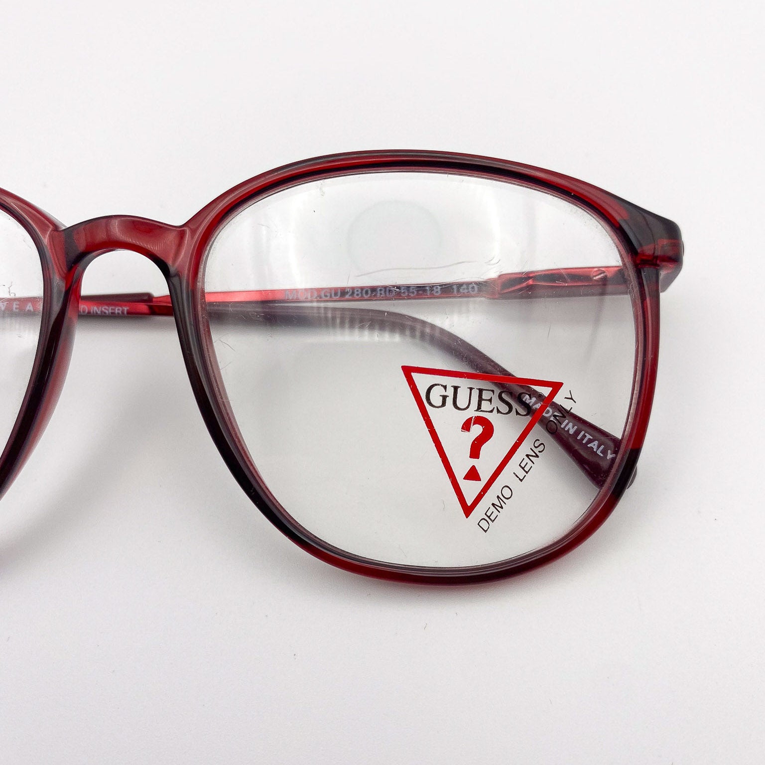 Vintage red eyeglasses with a clear lens featuring the Guess logo on a white background