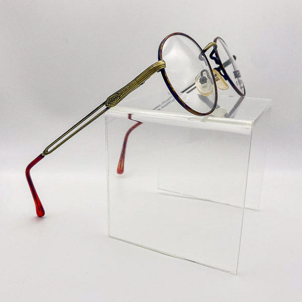 Eyeglasses with gold and tortoise frame on a clear stand against a white background
