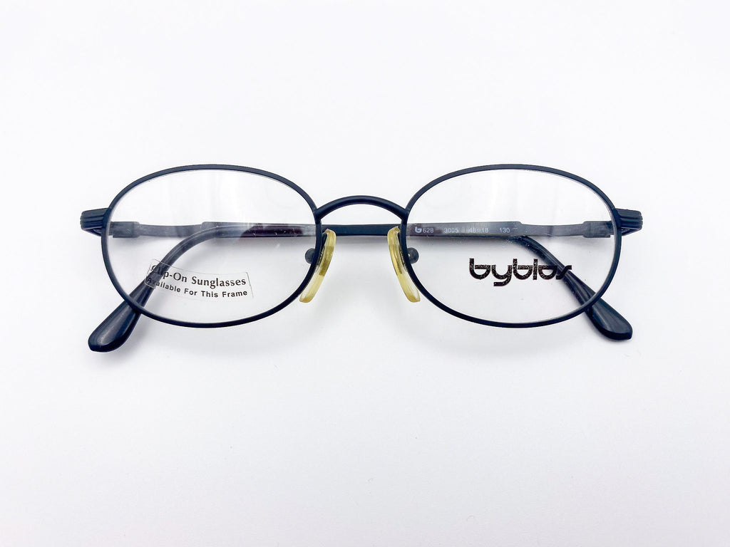 Oval round eyeglasses with black frame and 'byblos' branding on a white background