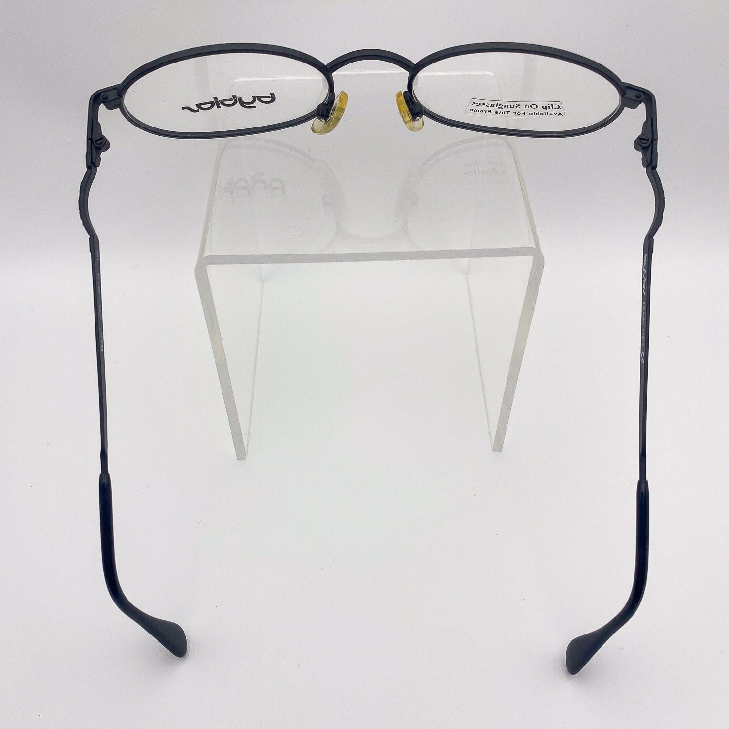 Black metal eyeglasses on a clear stand against a white background