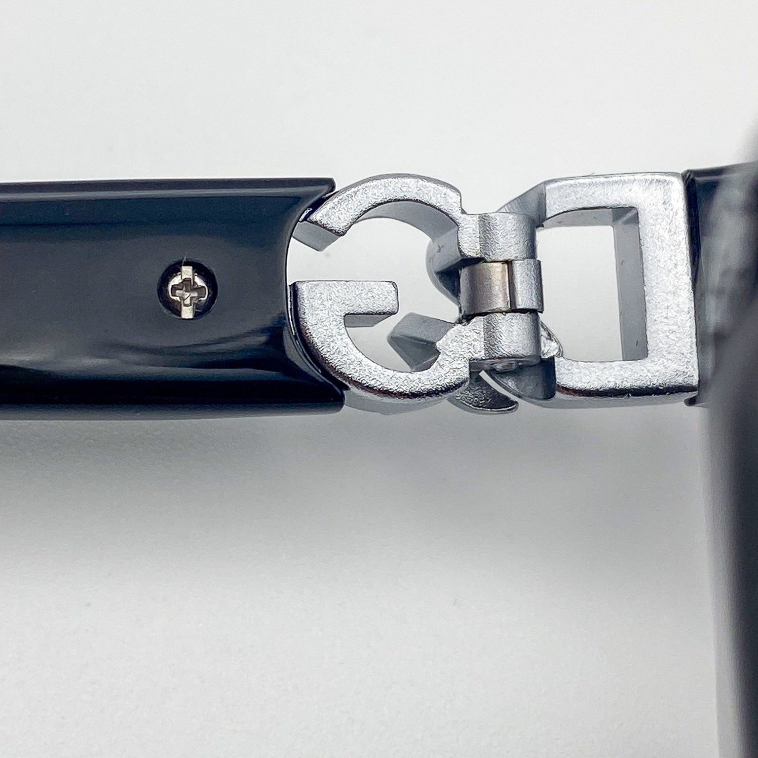 Close-up of a silver eyeglass hinge on a light gray background