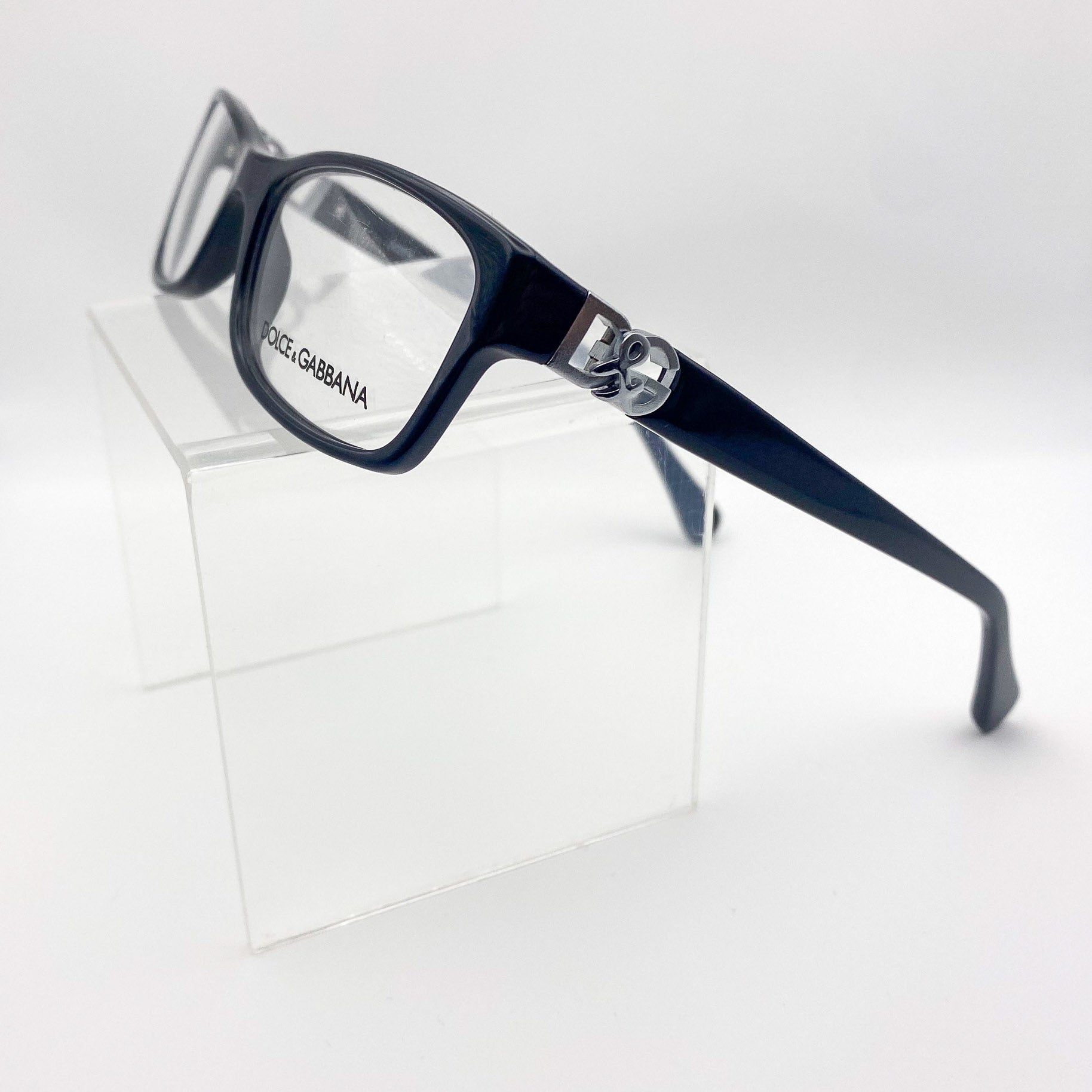 Black Dolce & Gabbana eyeglasses on a clear stand against a white background