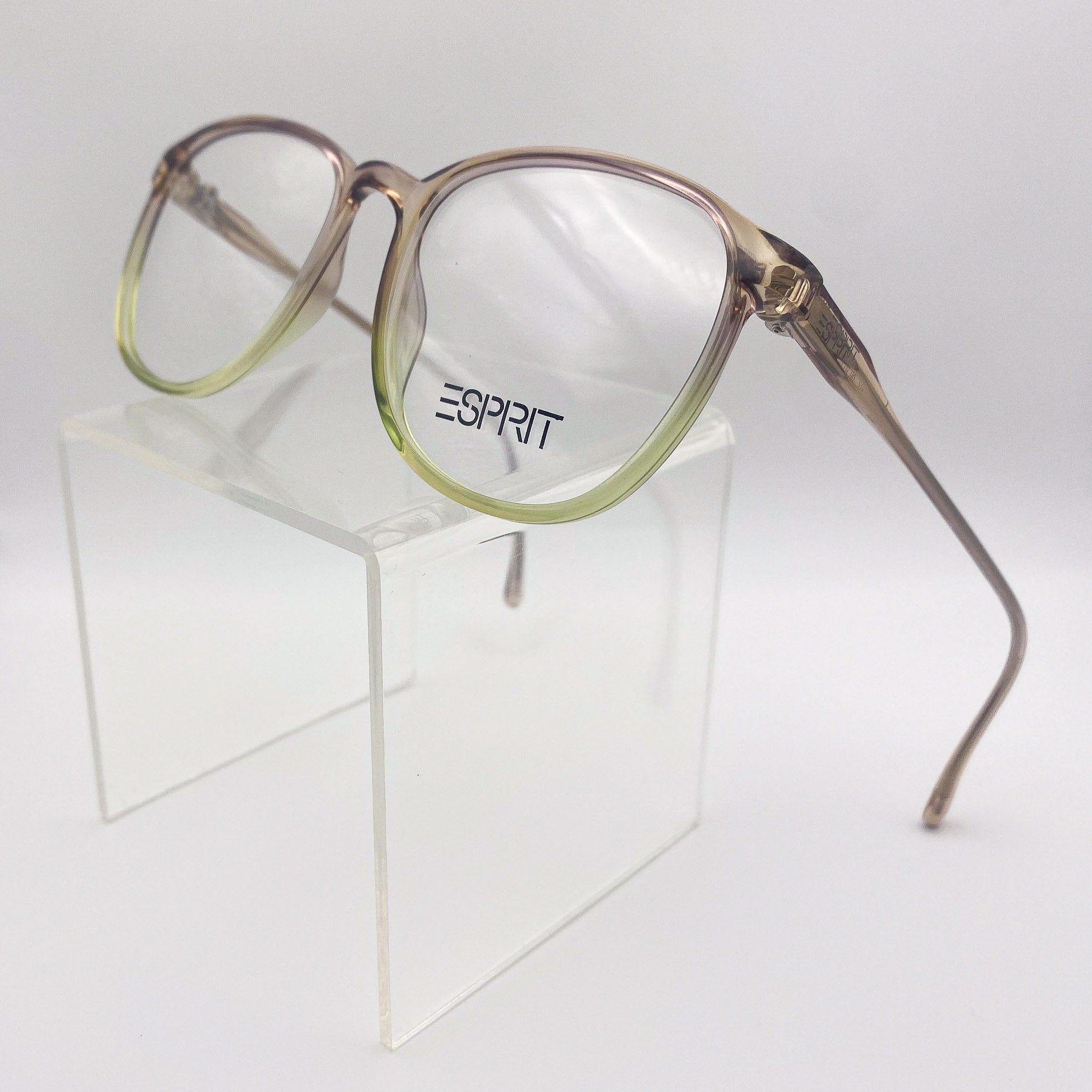 Brown and green fade eyeglasses with 'Esprit' logo on a clear stand against a white background