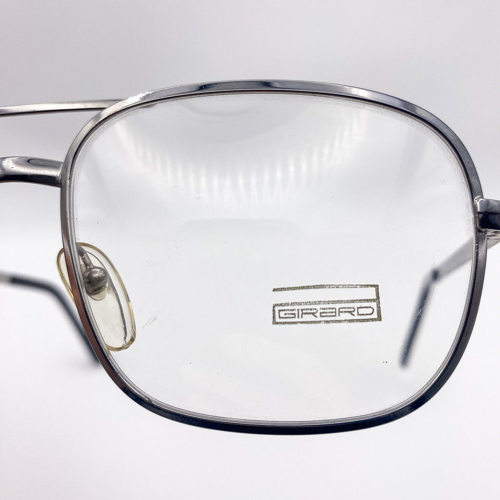 Close-up of a pair of glasses with 'Girard' branding on a light gray background