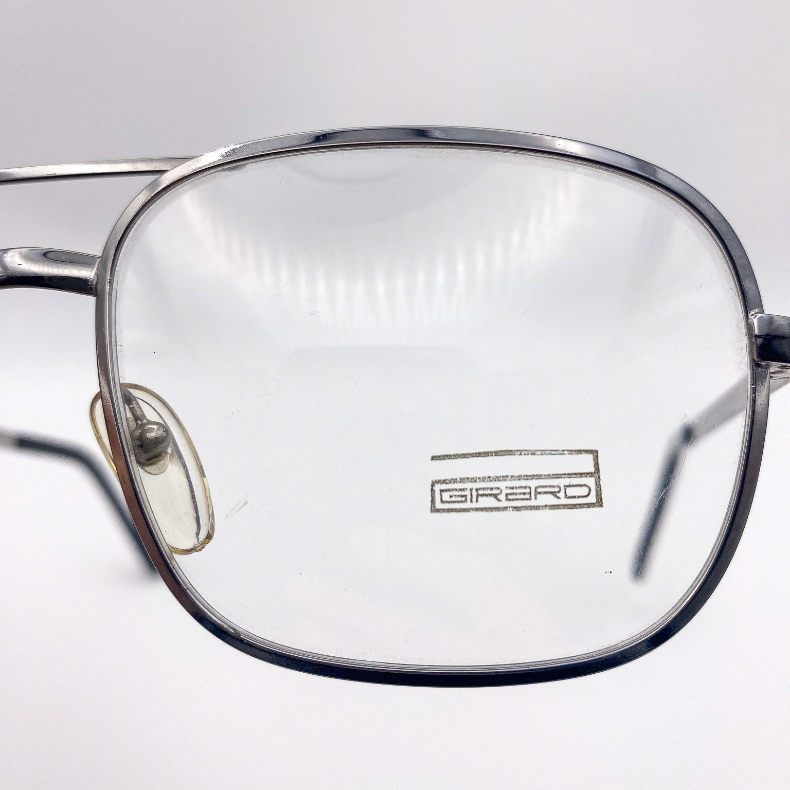 Close-up of a pair of glasses with 'Girard' branding on a light gray background