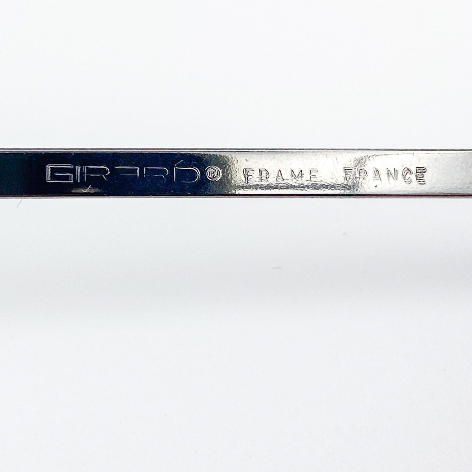 Metallic temple stem with 'Girard Frame France' engraving on a white background