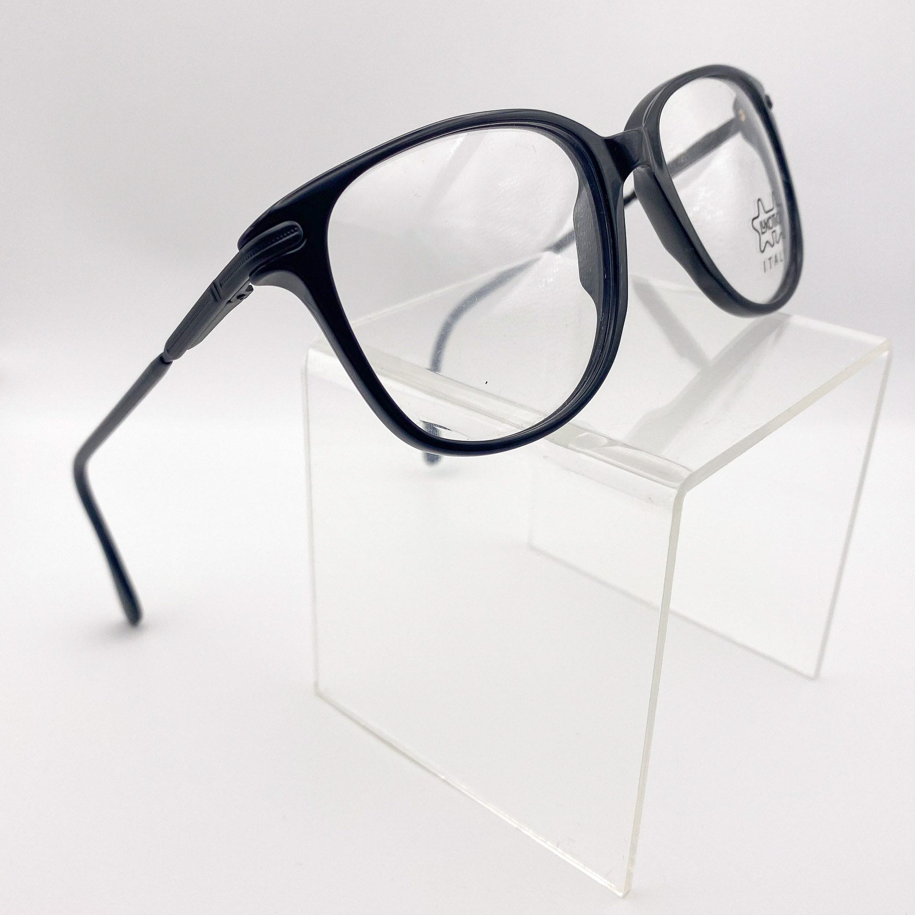 Black eyeglasses on a clear cube against a white background