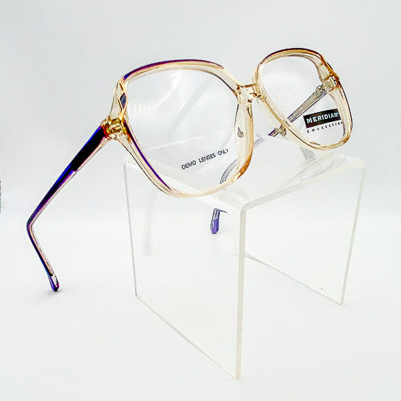Gold-framed eyeglasses on a clear stand with 'Meridian' branding.