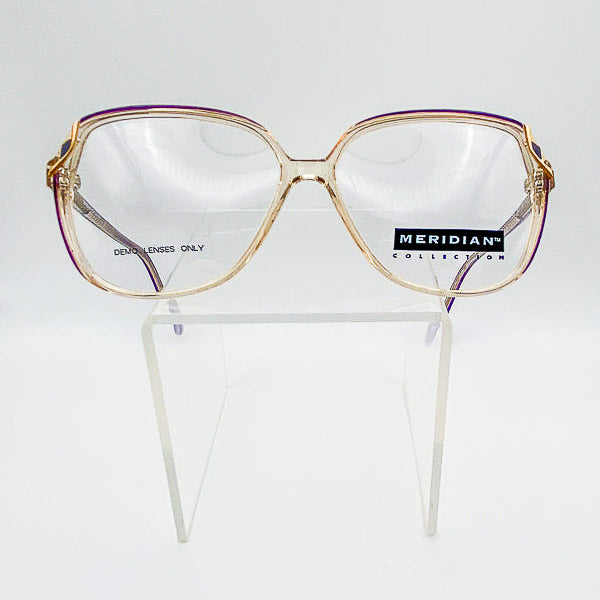 Gold-framed eyeglasses on a clear stand with 'Meridian Collection' label.
