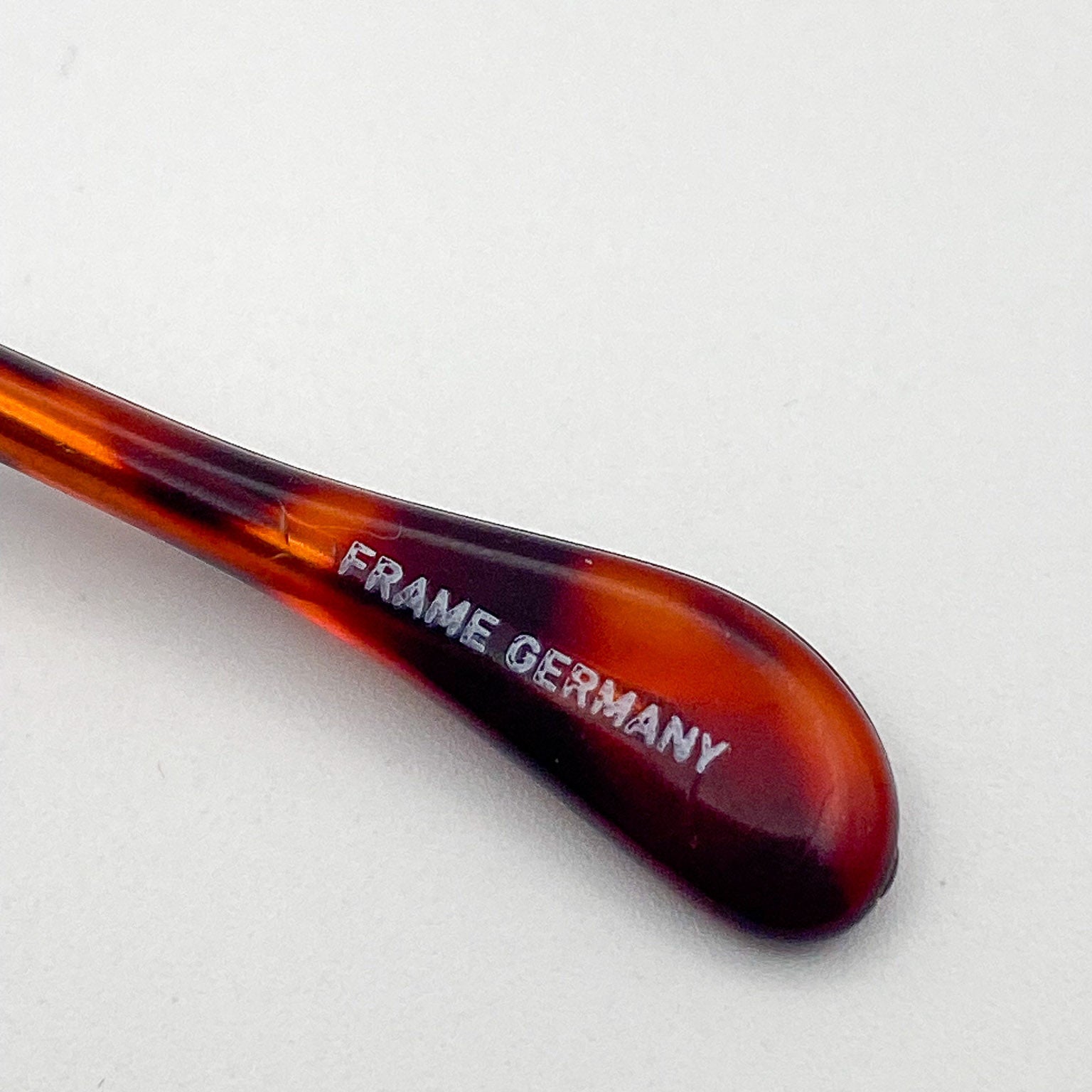 Tortoiseshell temple tip with 'FRAME GERMANY' engraving on a white background