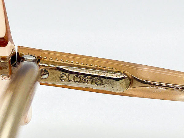 Close-up of a gold-colored temple with 'Elosta' branding on a white background