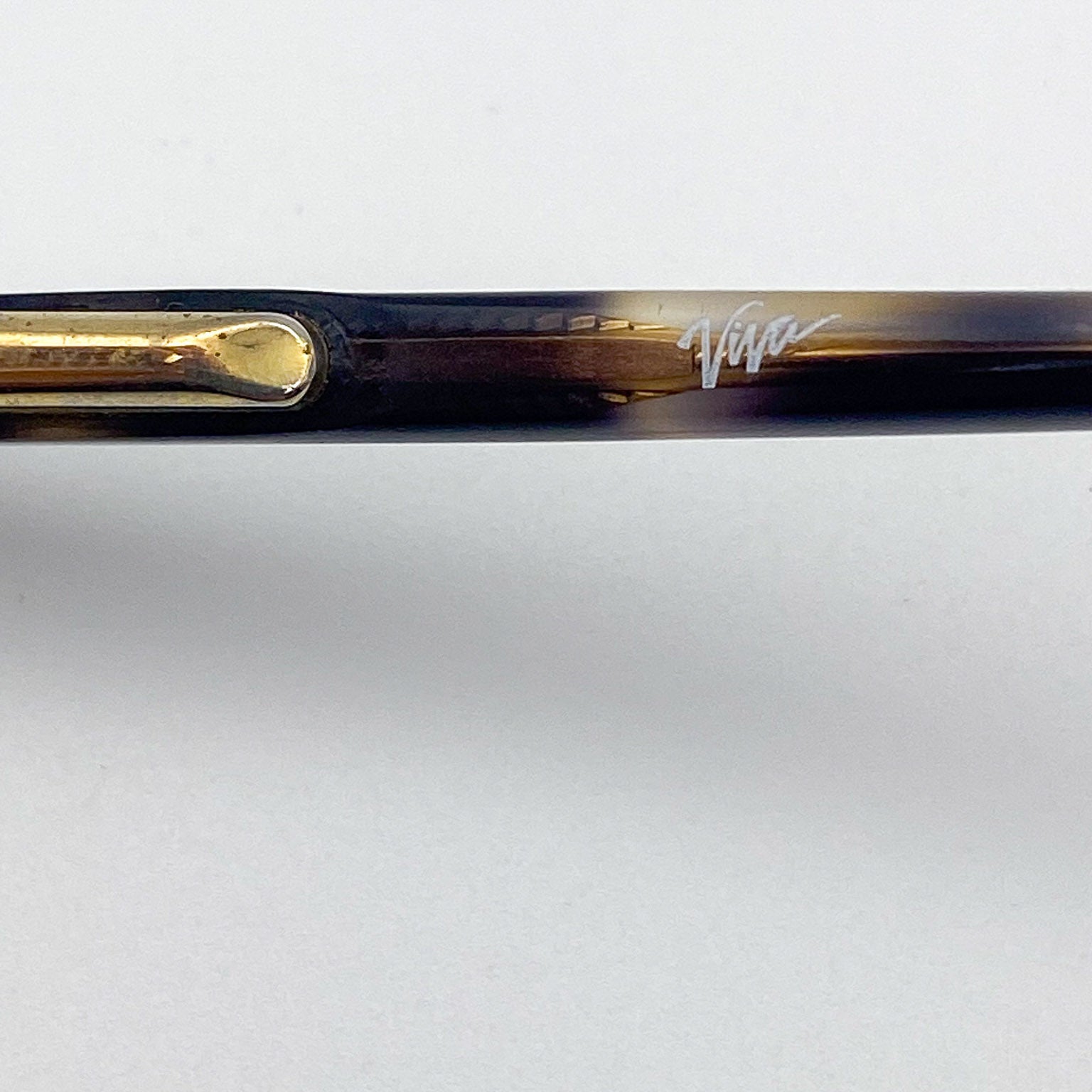 Close-up of eyeglasses with a tortoiseshell temple and gold accents on a white background