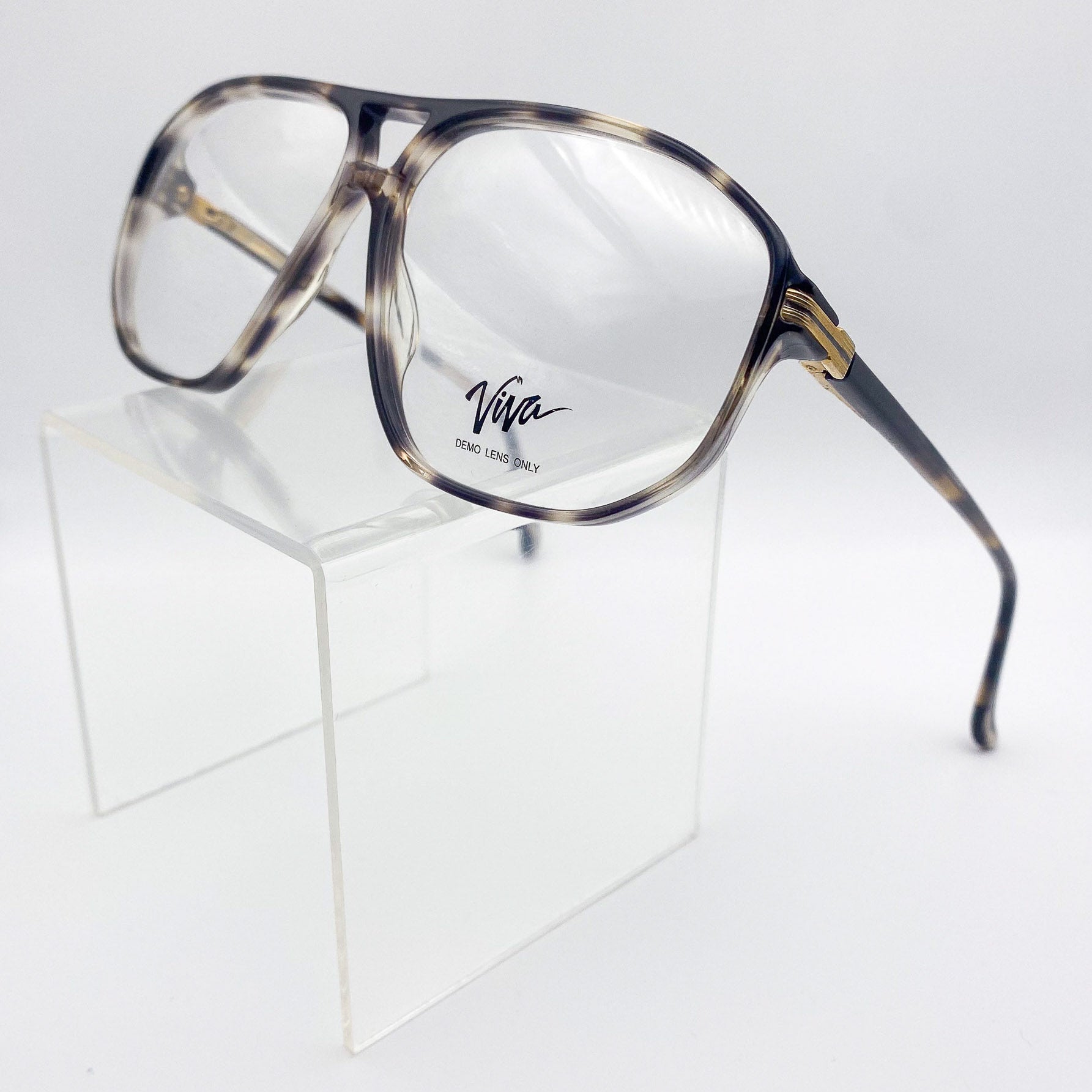 1980s eyeglasses with 'Viva' logo on a clear stand against a white background